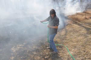 Bernita Sterling, owner of a rental home at 2325 Eddy Lane in LaPorte, turns her head from the heavy smoke as she keeps the fire at bay with her garden hose. The March 15 wildfire threatened at least three homes northwest of Fort Collins. Photo by Doug Conarroe, North Forty News