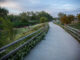 A paved trail along the Poudre River with wood post fencing and plants surrounding it.